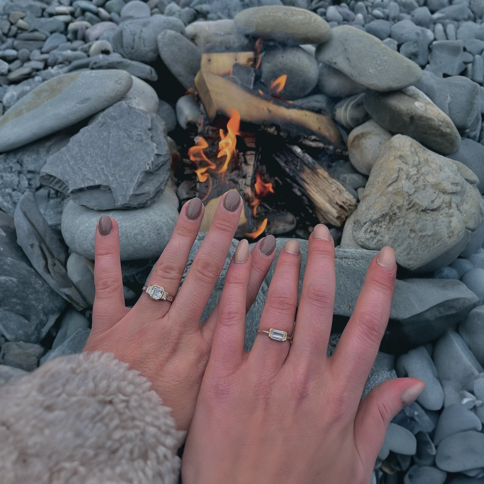 Custom engagement rings from Bogart's Jewellers, beautifully adorned on a couple's hands, glistening by a romantic campfire on a serene beach
