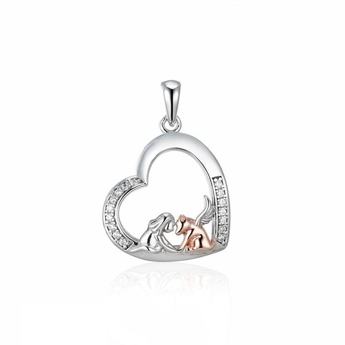 Sterling silver, heart shaped pendant with cubic zirconia accents along parts of the edge. Inside the heart a little girl is kneeling holding the paws of a rose gold-tone angel dog